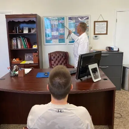 Dr. Toth pointing to a spine chart on his office wall while a patient listens from across the desk