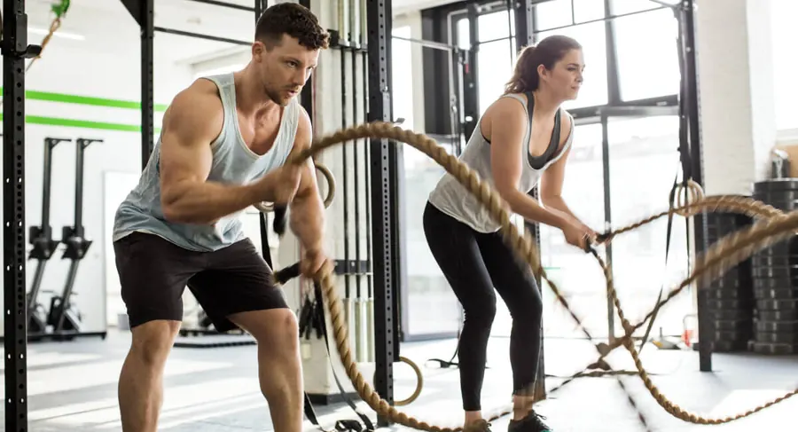 A man and a woman doing a battle rope warm-up workout in a gym